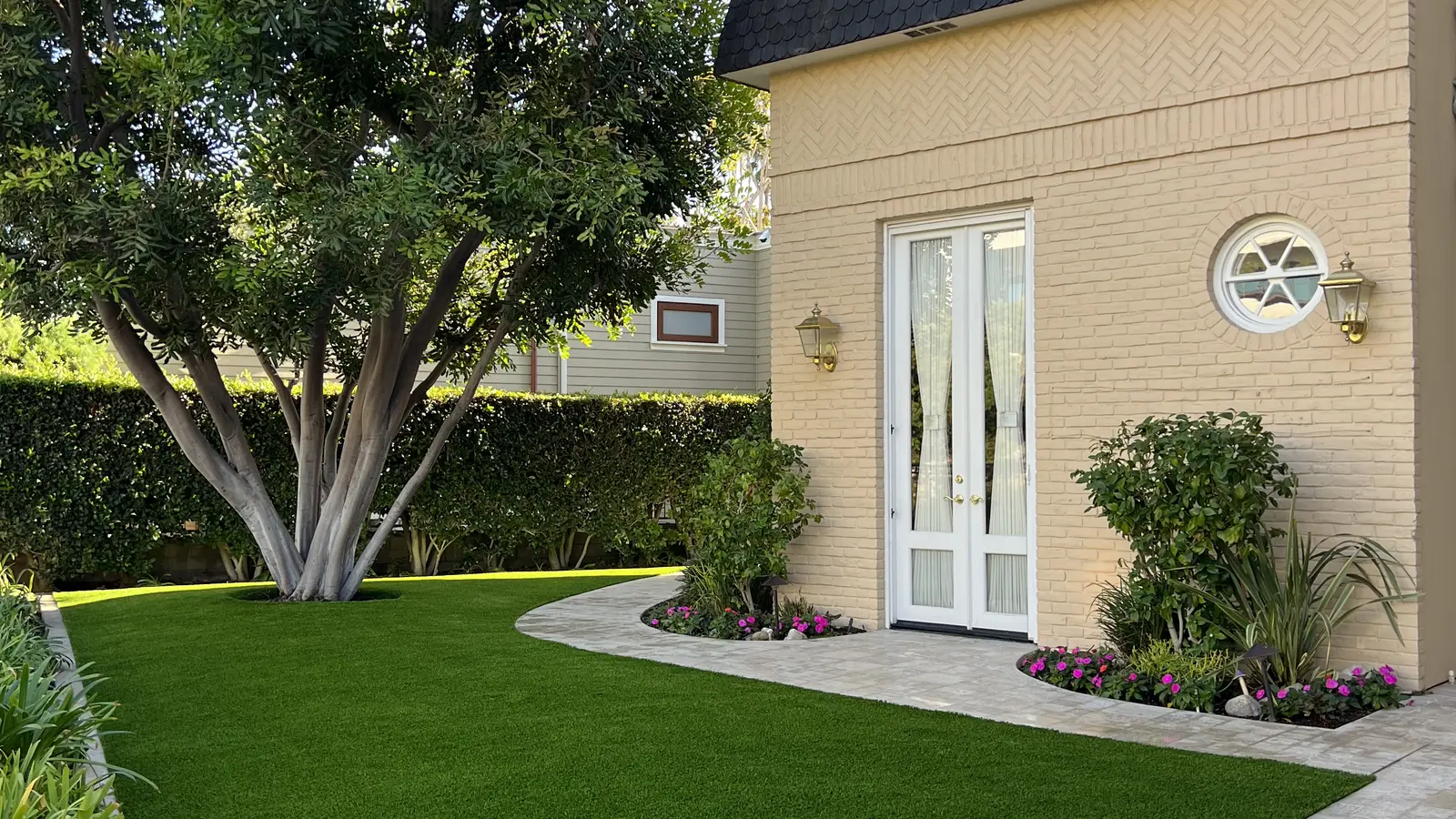 Artificial grass front garden with a curved paver border beside a cottage-style home