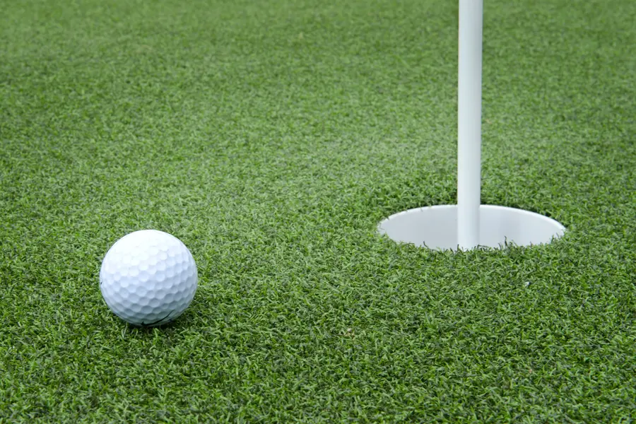 Golf ball resting beside a putting-green cup