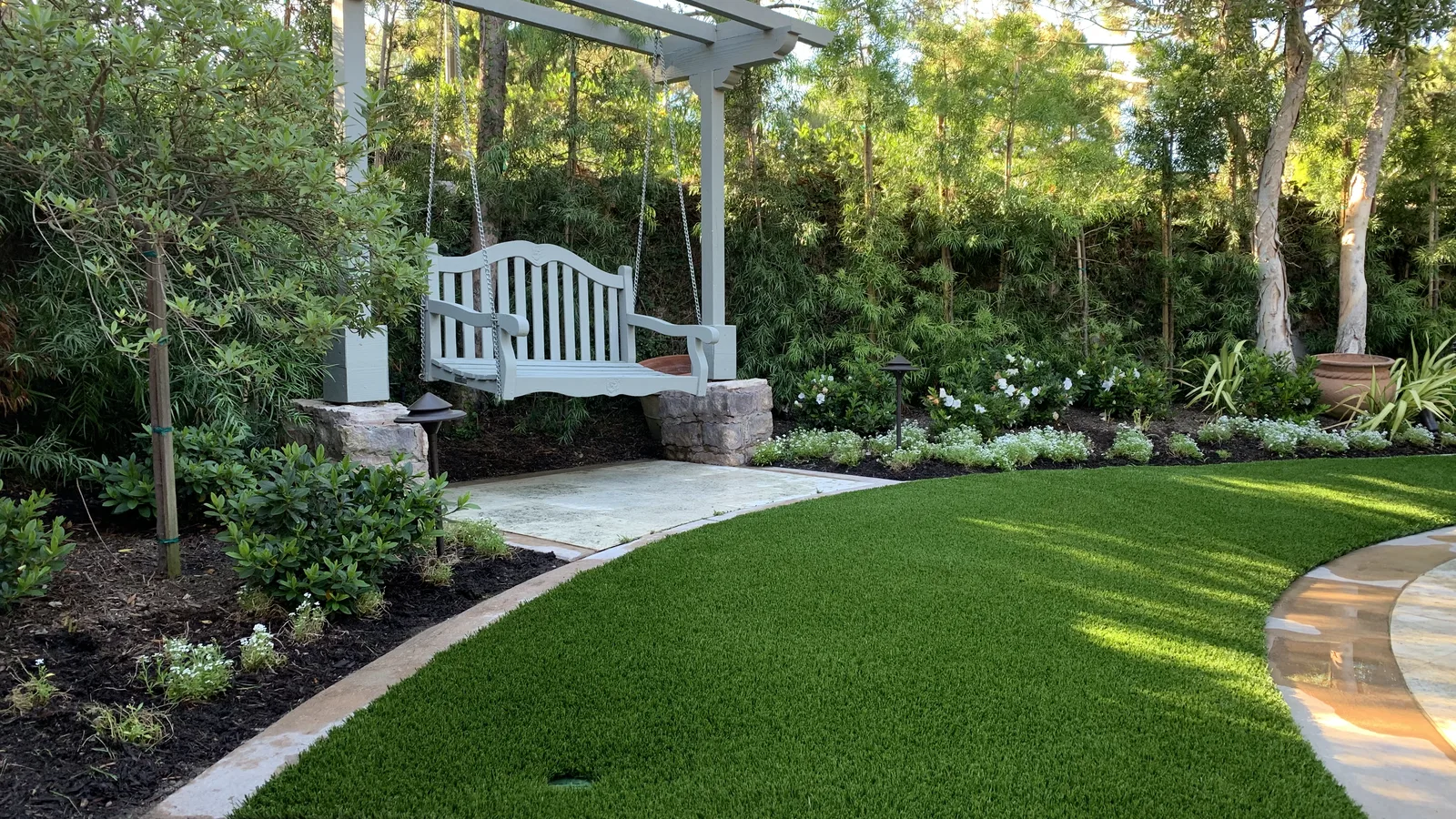 Lush artificial lawn beneath a white pergola swing