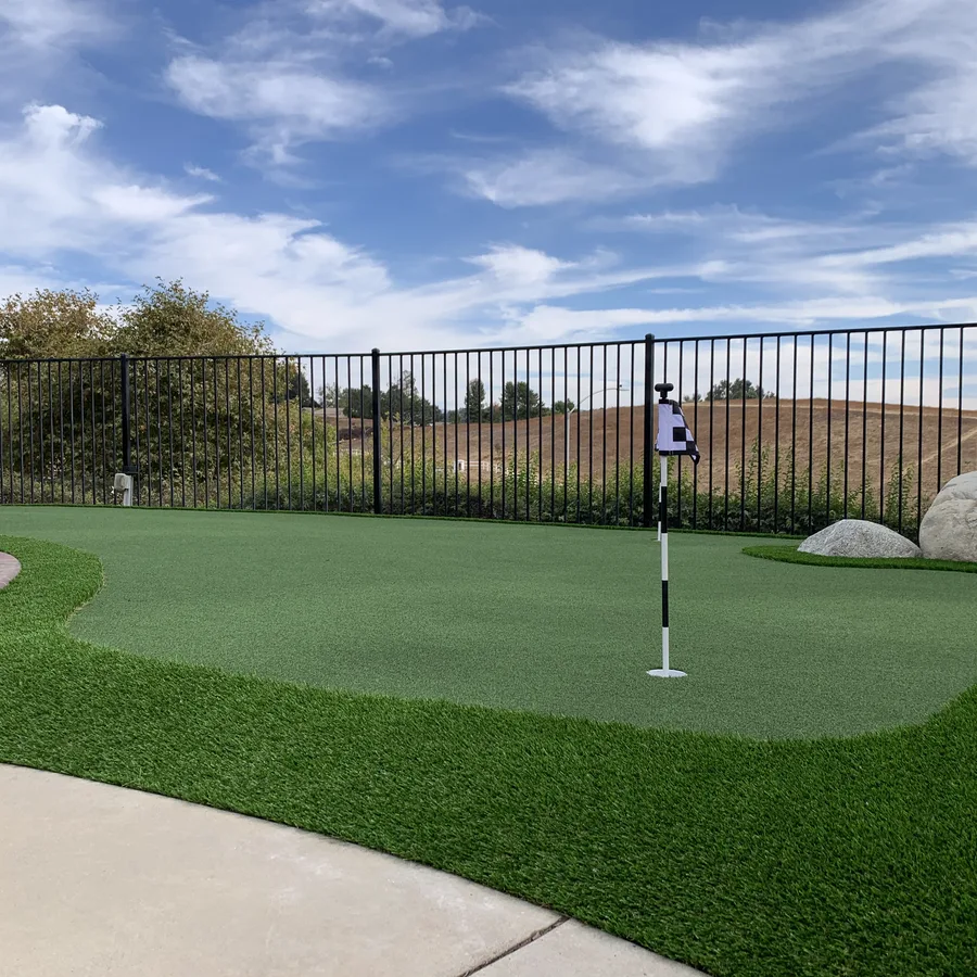 Backyard putting green along a black fence with a hillside view