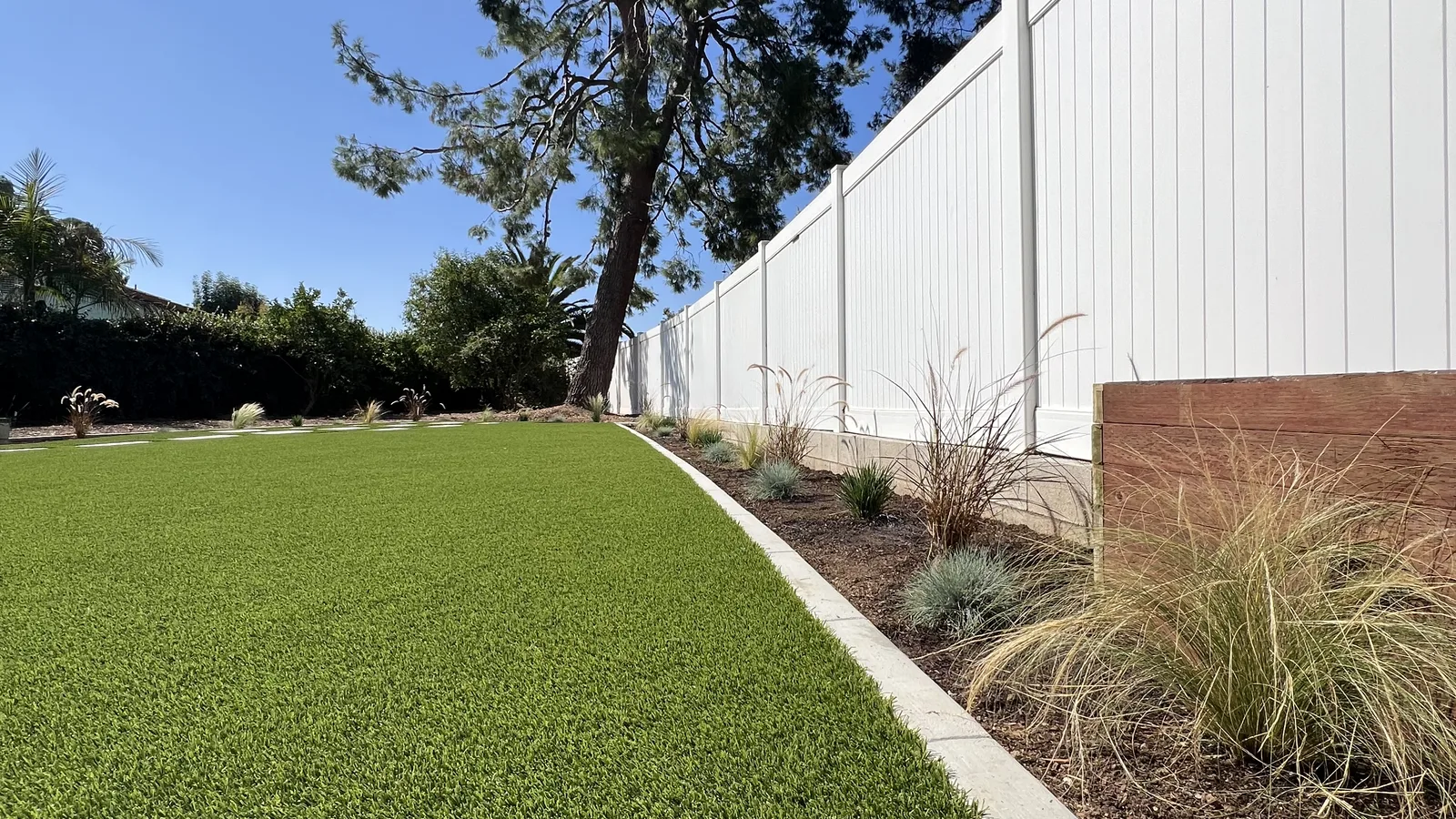 Clean side-yard artificial lawn along a white fence