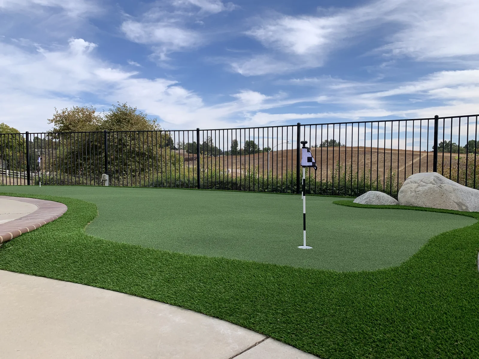 Backyard putting green along a black fence with a hillside view